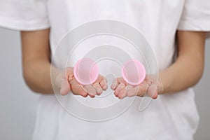 Close up of woman holding pink menstrual cups of different size in her hands on white background. Gynecology concept