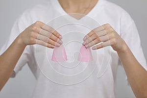 Close up of woman holding pink menstrual cups of different size in her hands on white background. Gynecology concept