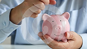 Close up of woman holding pink piggybank while woman putting coin in it for saving money and plan finance.