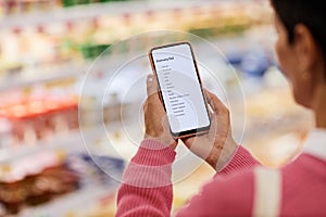 Close up of woman holding smartphone and reading shopping list in supermarket