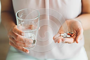 Close up woman holding vitamin pills in one hand and a glass of water in other