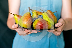 Close up woman holds plate with plums and pears