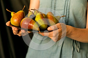 Close up woman holds plate with plums and pears
