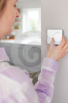 Woman At Home In Kitchen Turning Down Central Heating Thermostat To Save Energy And Money