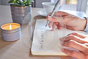 Close Up Of Woman At Home Writing In Gratitude Journal