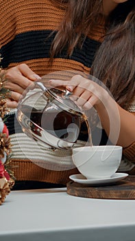 Close up of woman with kettle pouring tea in cup at home