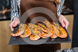 Close-up. A woman in the kitchen holds tiger prawns on a tray.