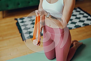 Close up of woman kneeling on yoga mat, holding resistance band for thighs