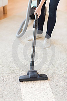 Close up of woman legs with vacuum cleaner at home