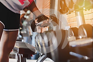 Close up woman are lifting dumbbells in the fitness room with dumbbells on rack