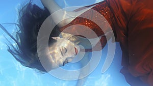 Close up of a woman in long red dress underwater, swimming, 4k