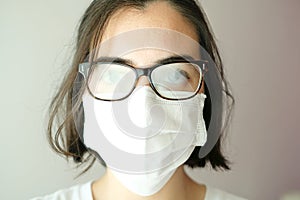 Close up of a woman looking at the camera with a white face mask during coronavirus outbreak with her glasses foggy from breath