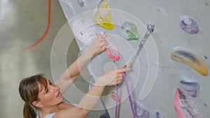 CLOSE UP: Woman loops her rope into a carabiner while holding on to a crimp hold