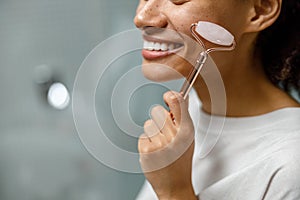 Close up of woman making face massage using roller in bathroom. Natural cosmetics concept photo