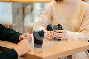 Close-up of woman and man sitting in cafe holding warm cups of coffee on table having fun conversation.