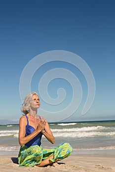 Close up of woman meditating while sitting on shore against clear sky