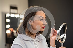 close-up of a woman paints her eyebrow with paint with a bone to a small make-up mirror.