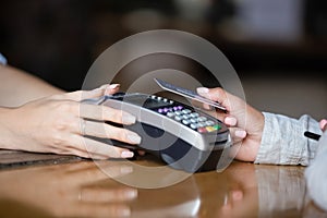 Close up woman paying by contactless card, terminal on bar counter