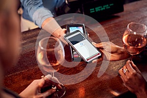 Close Up Of Woman Paying For Drinks At Bar Using Contactless App On Mobile Phone