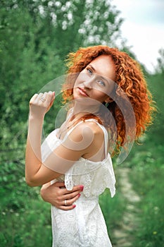 Close up.Beautiful red-haired girl in a white lace dress among the green park. A face with a natural make-up, a dreamy look of