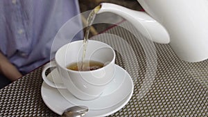 Close-up of woman pour the tea with teapot in cup.