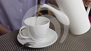 Close-up of woman pour the tea with teapot in cup.