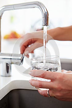 Close Up Of Woman Pouring Glass Of Water From Tap In Kitchen