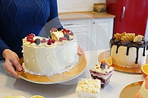 Close-up of woman putting berry sweet cake on the table to other desserts