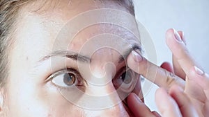 Close-up of a woman removing soft contact lenses from her eye against a white background.