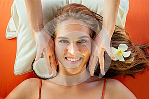 Close up woman on resort getting face spa treatment lying on a massage table and pillow with plumeria flower in hair and