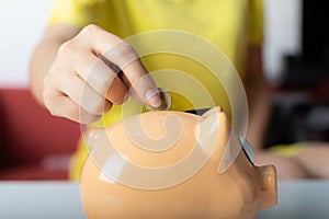 Close up woman right hand putting one coin into piggy bank