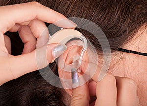 Close up of a woman`s ear and hands inserting a hearing aid