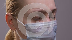 Close-up of a woman`s face, in a medical mask. The woman coughs.