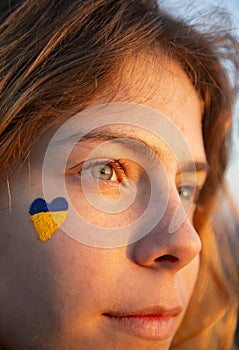 Close-up of a woman`s face with a painted yellow-blue heart on her cheek