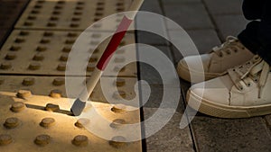 A close-up of a woman's feet with a tactile cane and a tactile tile indicating an obstacle.