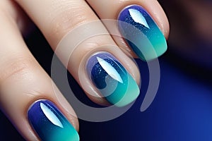 Close up of woman\'s fingernails with dark blue and turquoise ombre colored nail polish design