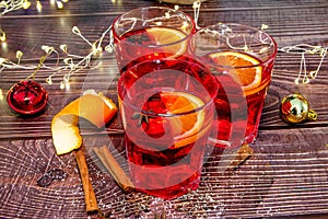 Close-up of a woman`s hand catching a glass of hot mulled red wine, on a wooden table with a Christmas tree in the background.