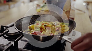 Close-up of woman`s hand cooking food in frying pan over the gas stove