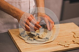 Close-up of a woman`s hand with a dough. The woman is cutting a cookie with a cookie cutter in the shape of a little.