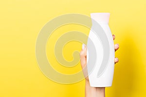 Close up of woman`s hand holding a bottle of cosmetics product at yellow background with copy space
