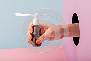 Close-up on woman`s hand holding a bottle of throat spray on blue and pink background