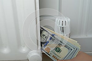 Close-up of a woman`s hand holding a calculator near radiator, temperature regulation in house with thermostat on white radiator,