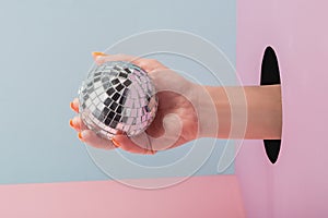 Close-up on woman`s hand holding a disco ball on blue and pink background