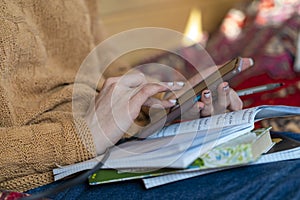 Close up of a woman& x27;s hand holding a mobile smartphone and using a pen while making notes in a notebook. Student