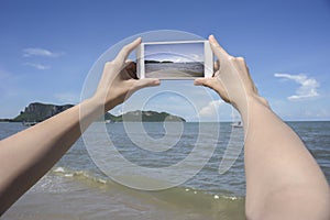 Close up of woman's hand holding smart phone, mobile, smart phone over blurred beautiful blue sea and fishing boat