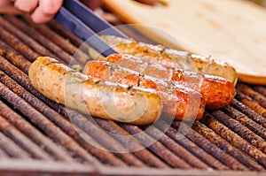 Close up of woman s hand holding a tongs turning the grilling sausages on barbecue grill. BBQ. Bavarian sausages