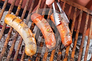 Close up of woman s hand holding a tongs turning the grilling sausages on barbecue grill. BBQ. Bavarian sausages