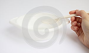 A close-up of a woman`s hand holding a white disposable plastic plate with a spoon for first courses, soup, broth and a top view.