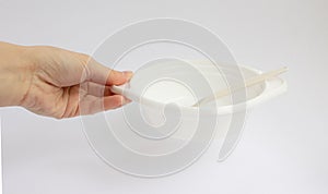 A close-up of a woman`s hand holding a white disposable plastic plate with a spoon for first courses, soup, broth and a top view.