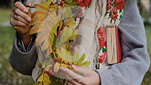 Close-up of a woman& x27;s hand leafing through the pages of a book. Autumn leaves are nested between the pages of the book